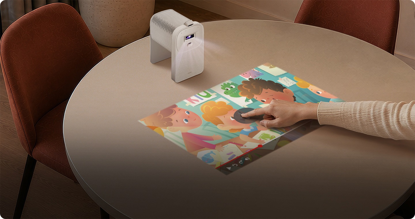 Le projecteur interactif The Premiere 5 de Samsung projette une vidéo pour enfants sur une table de salle à manger. Une personne appuie sur le bouton de lecture directement sur la table pour afficher le contenu.
