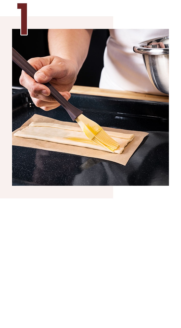 Paso 1. Una mano está pincelando cuidadosamente con huevo batido los laterales de una masa usando un pincel de pastelería.