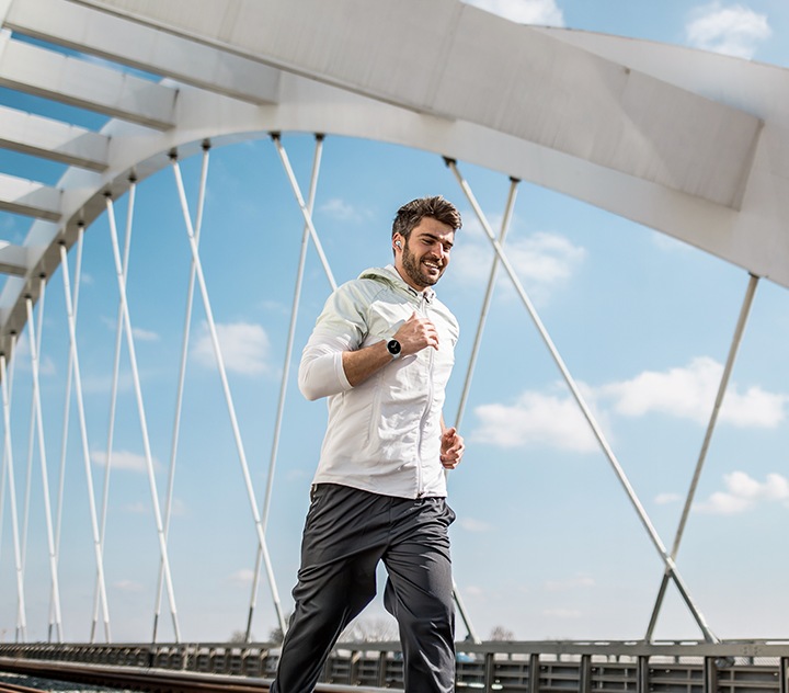 Mies juoksee sillalla Galaxy Watch -kello ranteessaan.