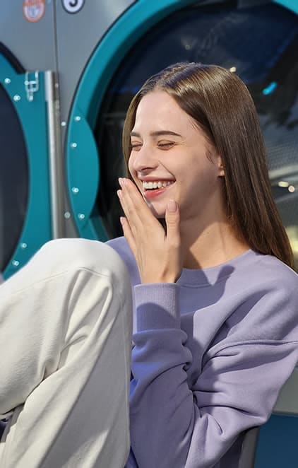 Une femme riant dans une laverie automatique, photographiée en mode portrait avec l’effet Flou activé.