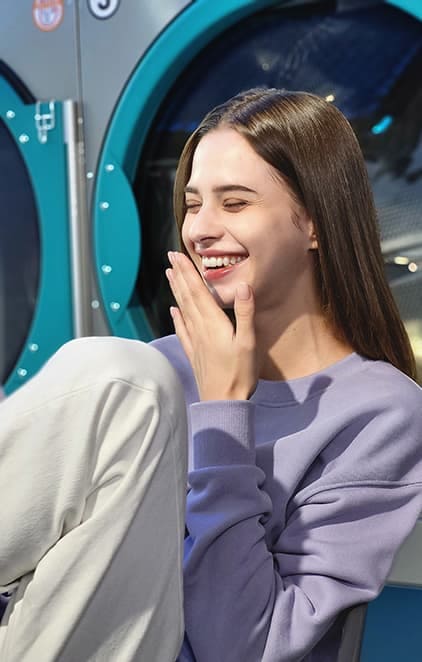 Une femme riant dans une laverie automatique, photographiée en mode portrait avec l’effet Studio activé.