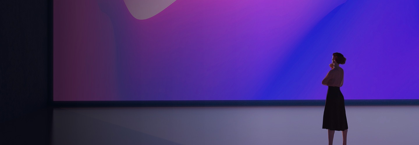 Pohled zezadu na ženu stojící na jevišti a hledící na velkou obrazovku, na které jsou zobrazeny jasně modré a fialové barvy.