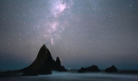 A beach rock formation in front of a starry night sky.