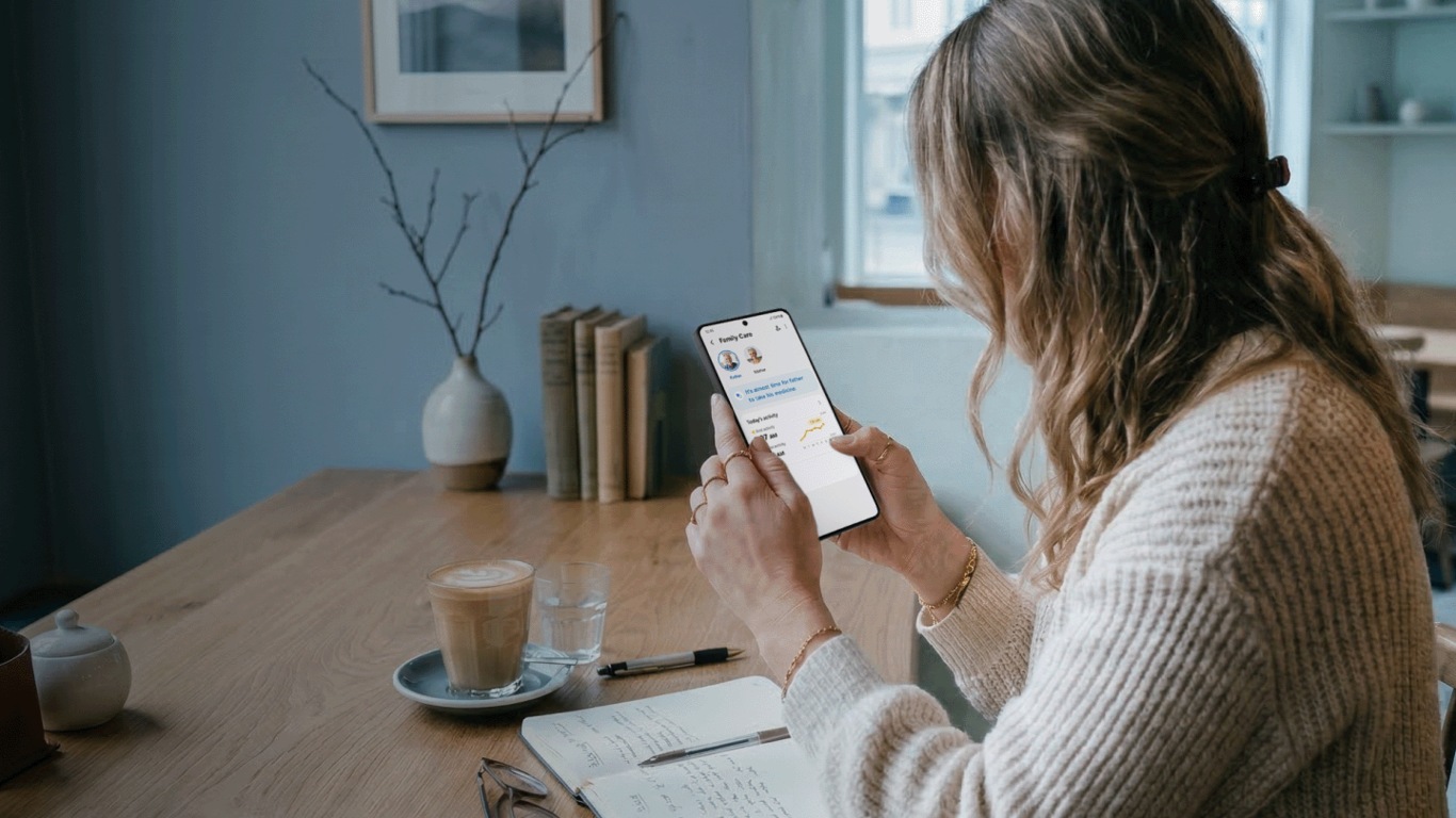 Woman sitting at a desk using a smartphone, with a coffee cup and books nearby