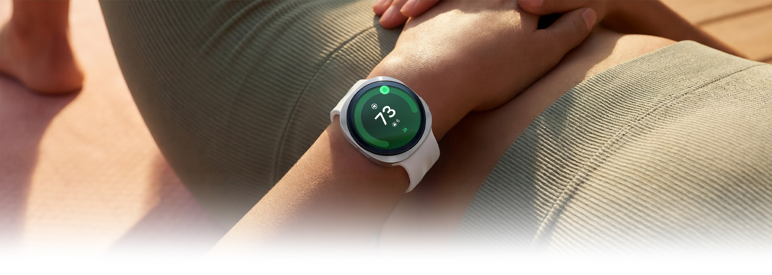 Egy hanyatt fekvő személy ezüst színű Galaxy Watch9 órát visel krém színű sportszíjjal a csuklóján, az óra kijelzőjén pedig 73-as Szívegészségügyi pontszám látható, kiemelve a Galaxy Watch9 szívegészségügyi funkcióit.