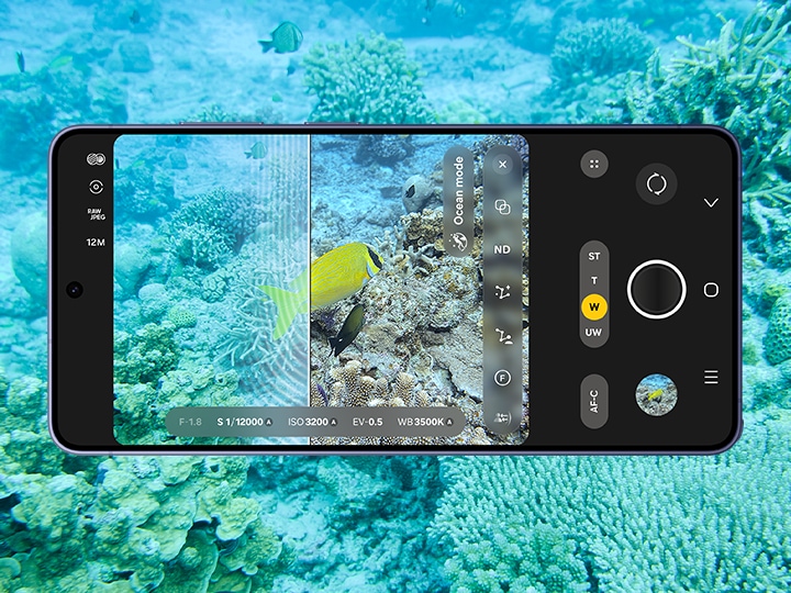 Galaxy S26 Ultra Cobalt Violet, dalam posisi horizontal dengan adegan bawah air di latar belakang. Aplikasi Expert RAW di layar utama mengambil foto adegan bawah air tersebut. Sebuah garis menunjukkan perbedaan antara foto asli dan foto yang telah dioptimalkan; rona biru dikurangi sehingga menghasilkan warna yang jernih dan realistis.