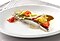 A fillet of trout has been plated on the white plate beautifully with colorful vegetables on top.