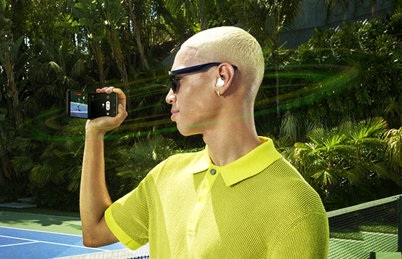 A young man holding his Galaxy Z Flip4 with the Galaxy Buds2 Pro in his ears is recording a moment using 360 Audio Recording.