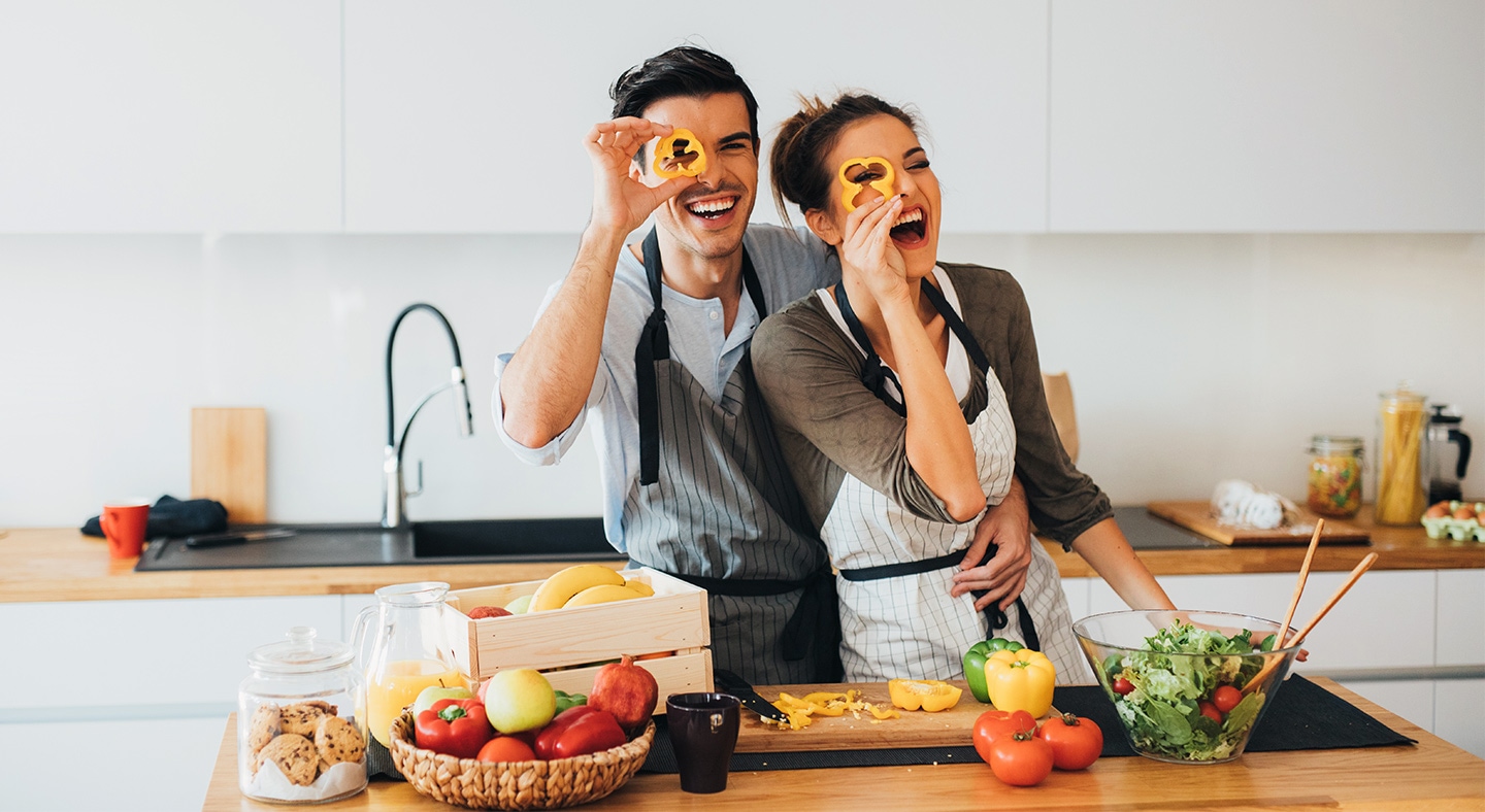 Young couple holding sliced bell pepper in front of their eyes and having fun as they're cooking in the kitchen. 