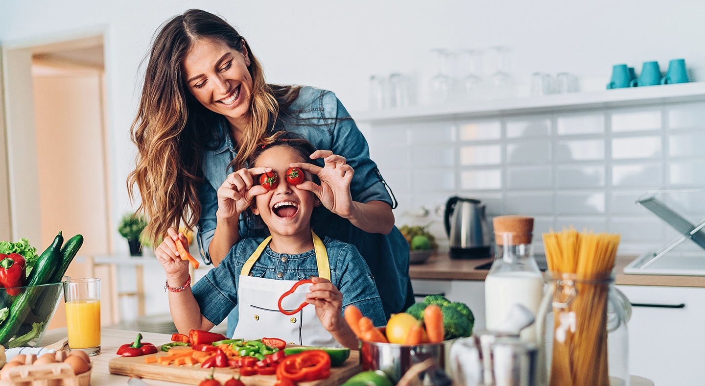 Happy mother and daughter playing with cherry tomatoes while making salad in the kitchen.