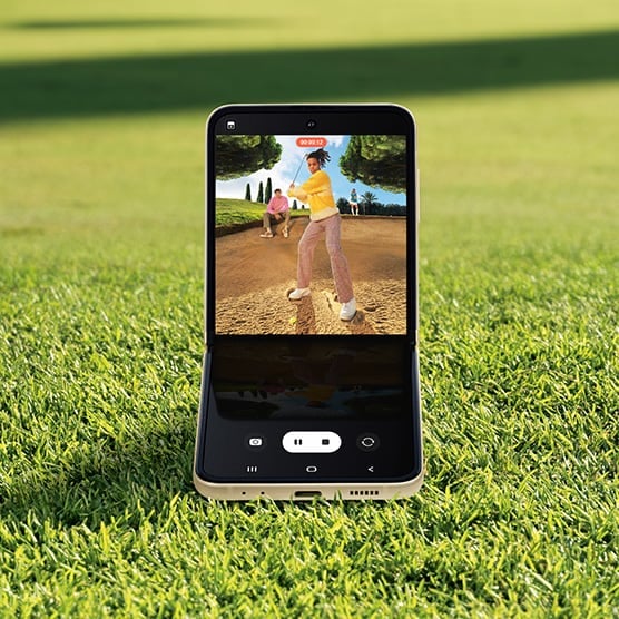 Galaxy Z Flip3 5G in Flex mode. The camera is seen on the Main Screen in Video mode and is recording a video of the man swinging his golf club.