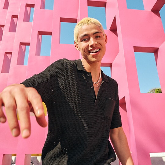 Man in a black shirt poses at an extreme angle for a selfie from the waist up against a bright pink structure. With Flex mode, he can pose from a distance without having to hold the phone.