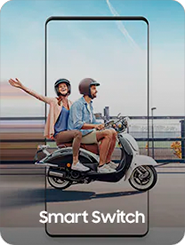 A man drives a scooter against a city backdrop. A female behind him reaches out and faces the camera. Both are wearing helmets.