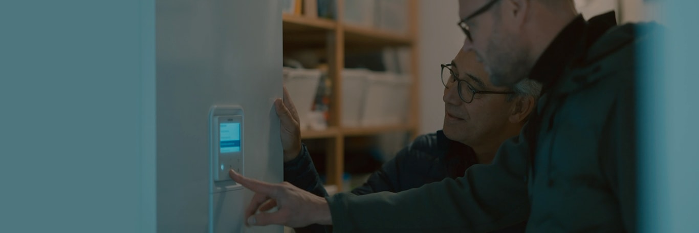 پانێڵی کۆنتڕۆڵکردنی سپلیتی Samsung کە لەسەر دیوار دامەزراوە لەلایەن پیاوێکەوە کاریپێدەکرێت، پیاوێکی دیکەش لە تەنیشتییەوە وەستاوە و چاودێری دەکات.