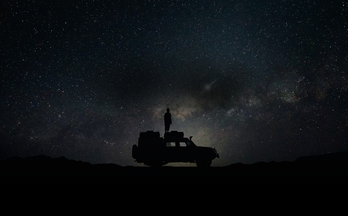 A person standing on top of their car against a starry night sky