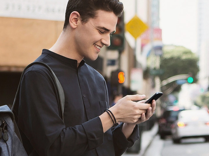 The man is smiling at his cell phone on the road.