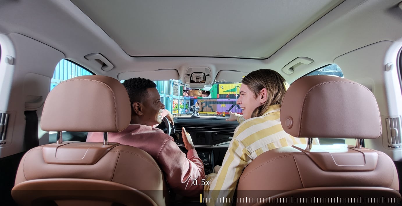 Due amici seduti sui sedili anteriori di un’auto. Avanzando con lo zoom si vede un uomo attraverso il parabrezza, che balla ascoltando la musica con i suoi Galaxy Buds.