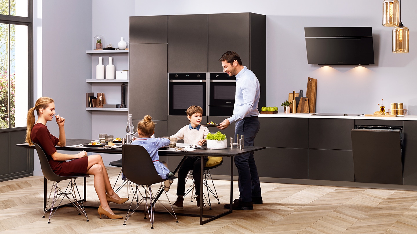Una famiglia sta cenando in una cucina con gli elettrodomestici neri.