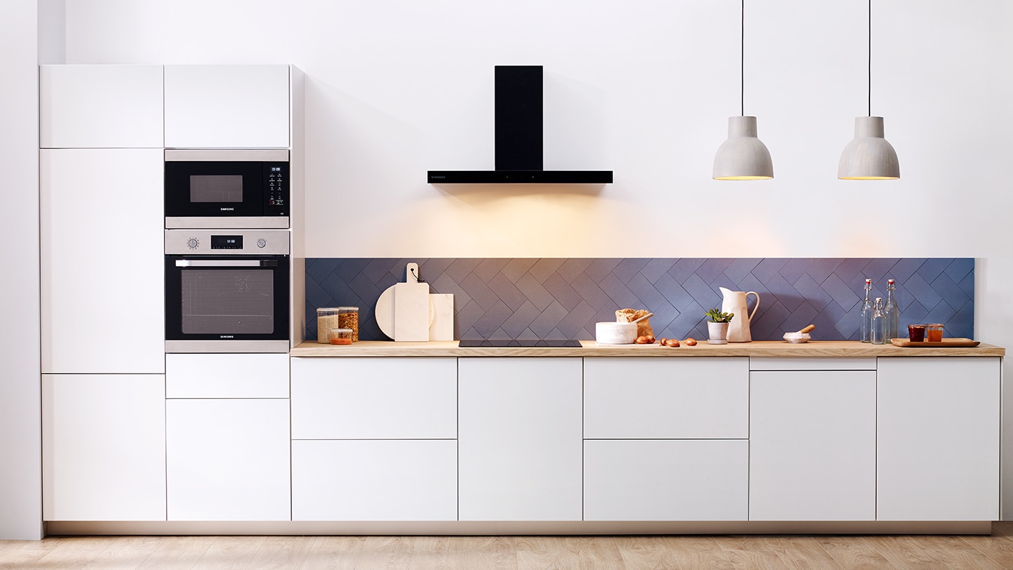 Un intero set di elettrodomestici da incasso Samsung come frigoriferi, forni, forni compatti, piani cottura lavastoviglie e cappe sono installati in una cucina bianca premium.