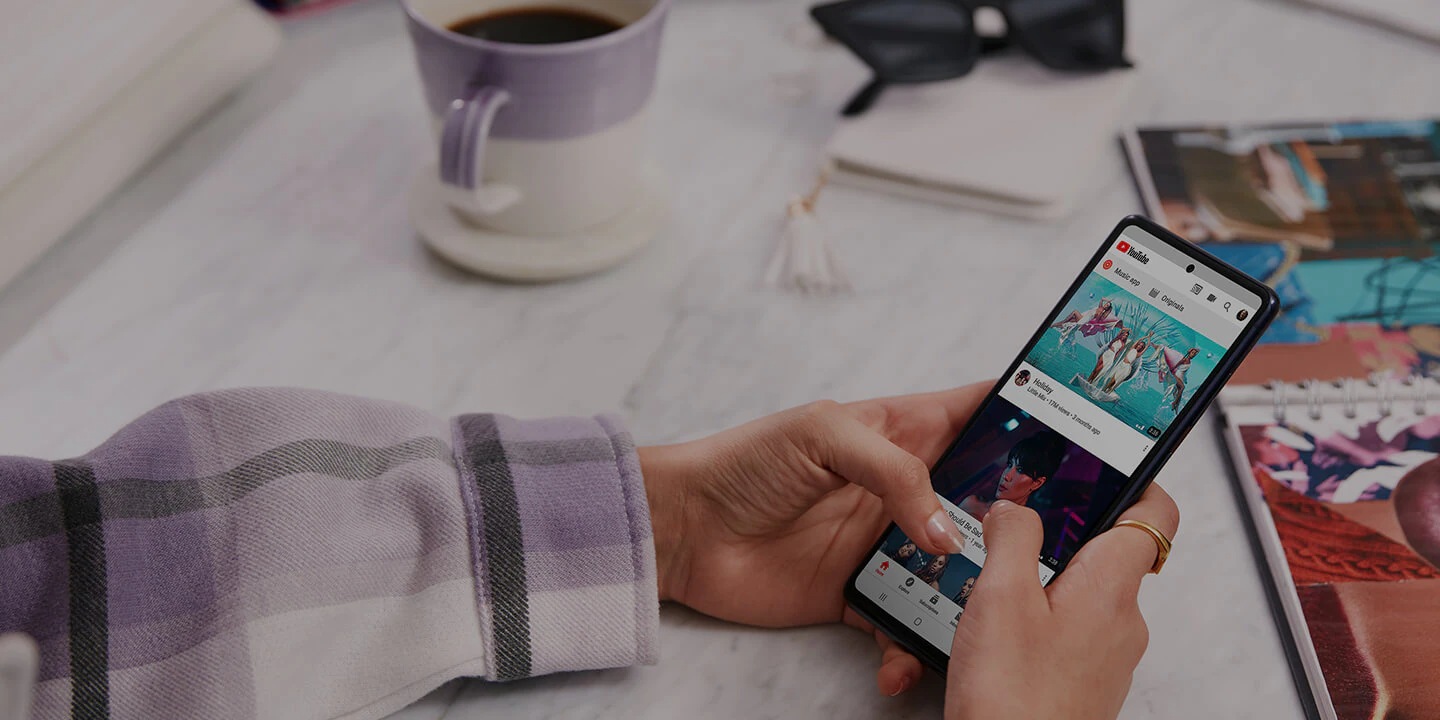 Un smartphone Samsung Galaxy negru care arată un serviciu de streaming video pe ecran cu o ceașcă de cafea și o revistă pe masă 