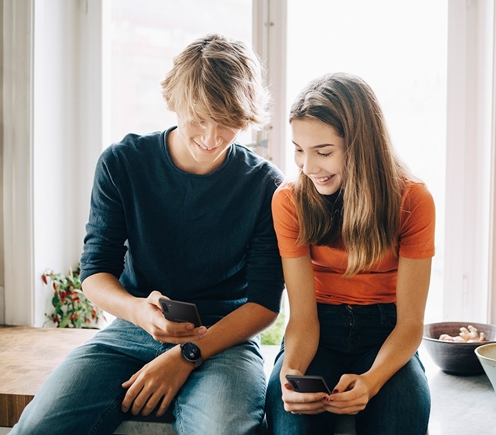 自分のGalaxy Watch（ギャラクシーウォッチ）のテーマとスマートフォンのテーマがマッチしていることを女性に示す男性。