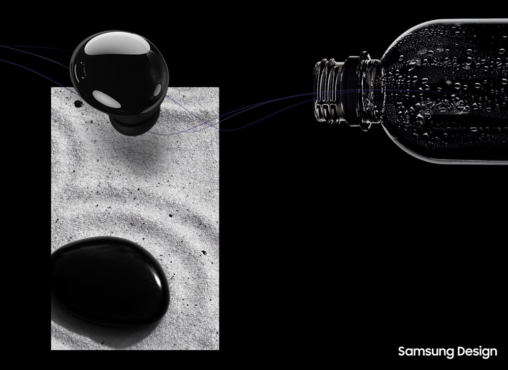 砂の上に黒く楕円形の石とGalaxy buds pro(ギャラクシーバズプロ)ファントムブラックが上下に並んでいる。Galaxy Buds Proの横には、気泡の入ったプラスチックペットボトルに吸い込まれていきそうな絵が描かれている。