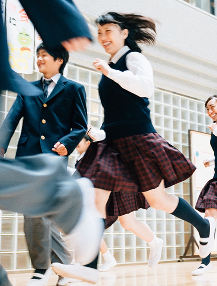 制服の高校生たちが学校の構内を楽しそうに全力で走っている。これからの新生活に溶け込むスマートフォンの魅力を表現している。