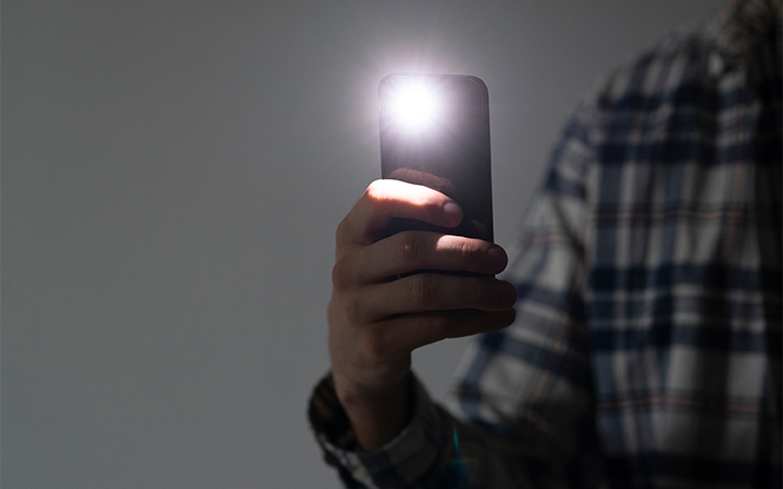 [男性が片手に持ったスマートフォンのライトを起動し光をこちらに見せている。]