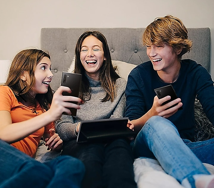 Трое друзей, сидя на диване со своими смартфонами, смеются и делятся информацией об эксклюзивных играх в Galaxy Store.