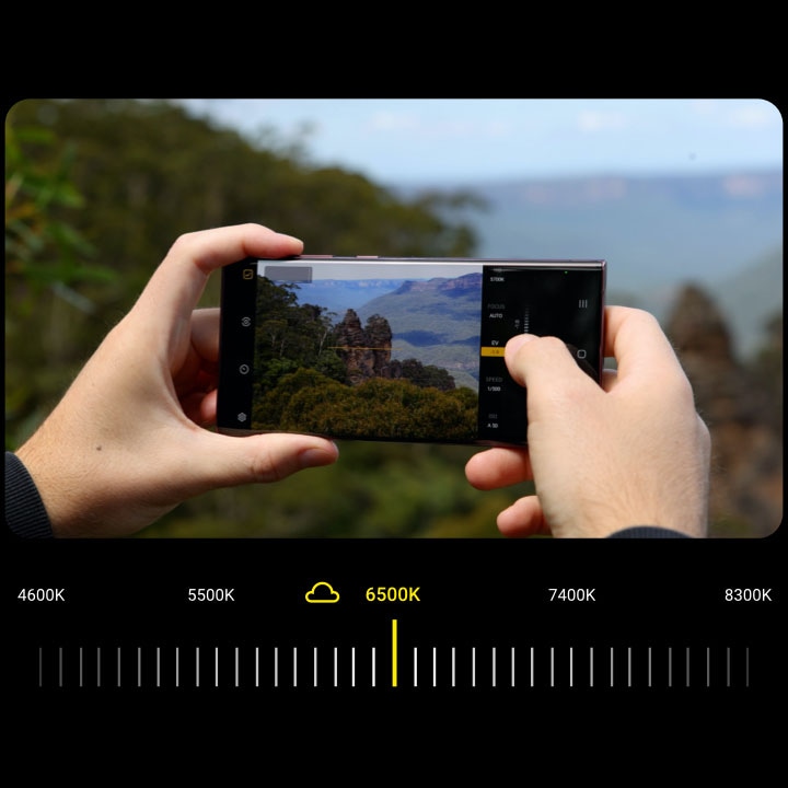 A photographer looks through the viewfinder of the Expert RAW app on a Galaxy S22 Ultra to capture a natural outcropping of rock in the Blue Mountains National Park in New South Wales, Australia. He drags a slider to adjust the white balance of the shot, making it bluer and more atmospheric. 