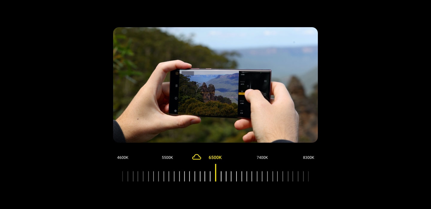 A photographer looks through the viewfinder of the Expert RAW app on a Galaxy S22 Ultra to capture a natural outcropping of rock in the Blue Mountains National Park in New South Wales, Australia. He drags a slider to adjust the white balance of the shot, making it bluer and more atmospheric. 