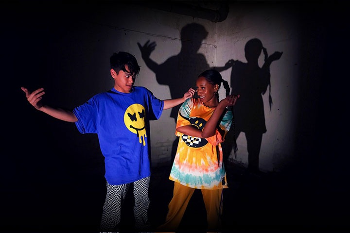 Two dancers in low light gesturing toward each other and creating shadows