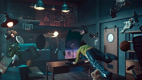 Человек и вещи в комнате плавают вокруг монитора. Монитор повернут вертикально, и на экране монитора поезд направляется к док-станции.