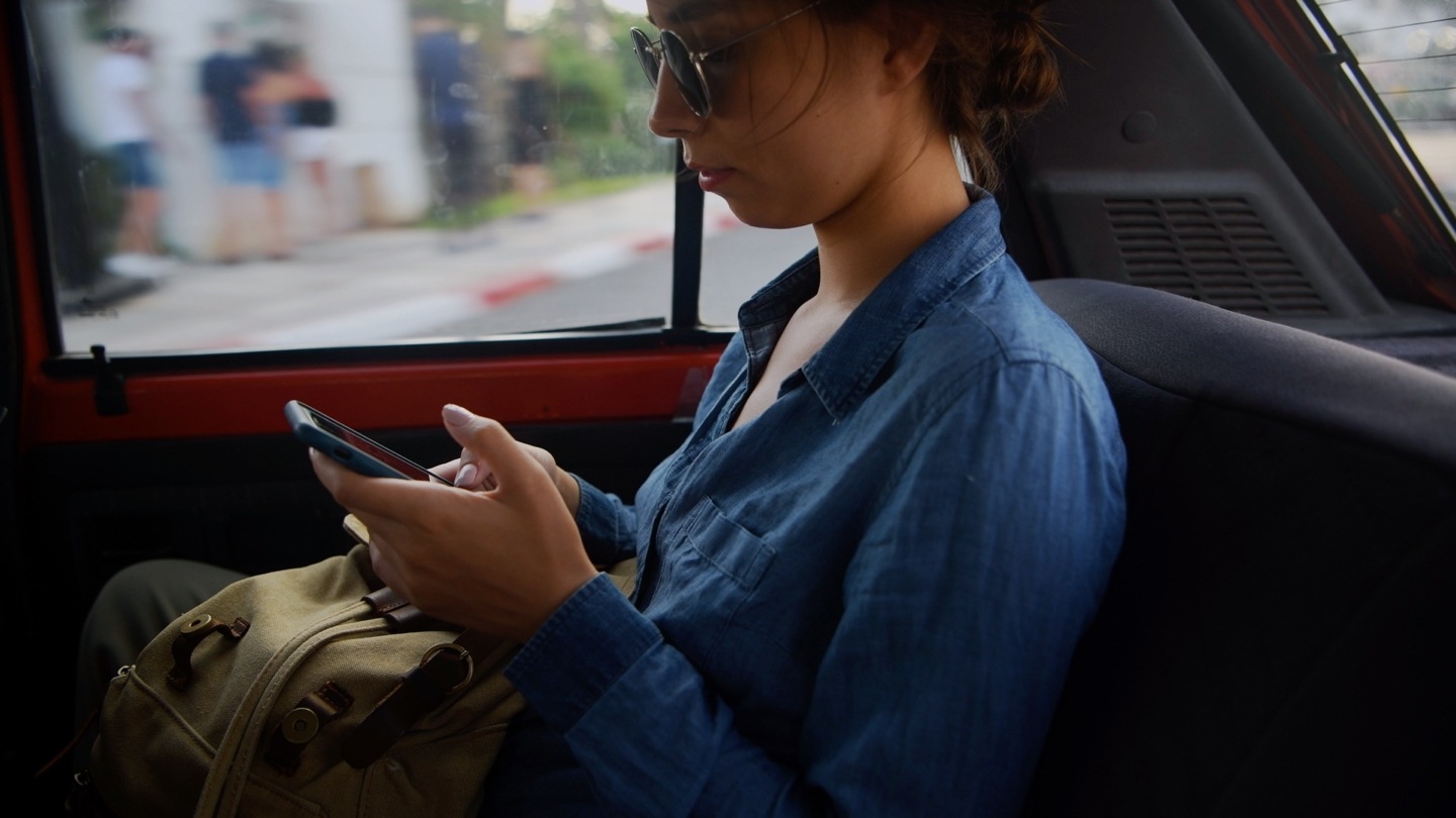 A movie that shows side view of passenger woman riding in car and messaging  with smartphone