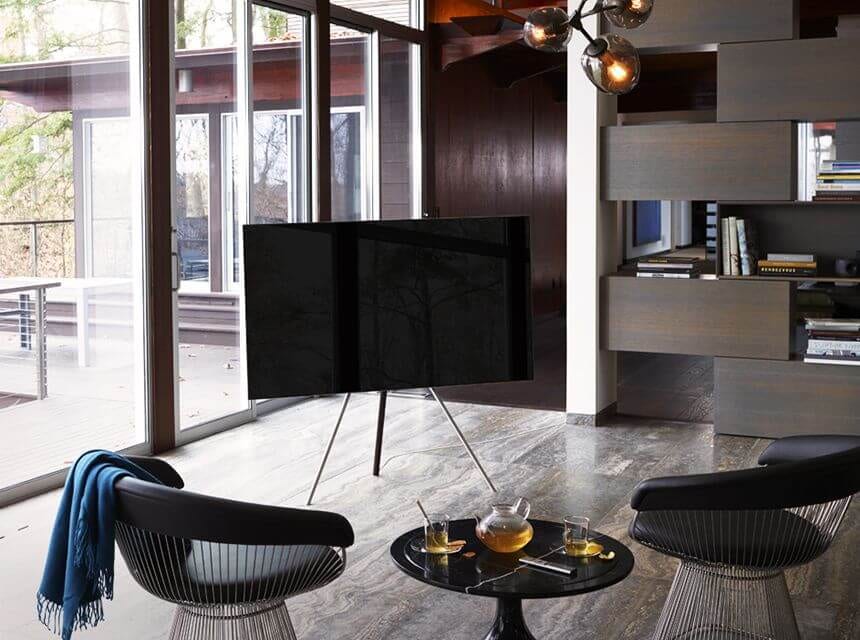 There are a sofa and black dog in a living room with the wide-open view outside. QLED TV is hung on the wall in front of the sofa, and there is a small rack at the bottom of the TV.