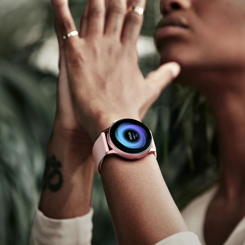 A woman practicing yoga with hands together and a Galaxy Watch active2 in Pink Gold on her wrist that displays breathing exercises on the watch GUI, after which a separate person is shown sleeping with a Galaxy Watch active2 on the wrist that tracks sleeping patterns and compares them to others in the same age bracket as displayed on the watch GUI.