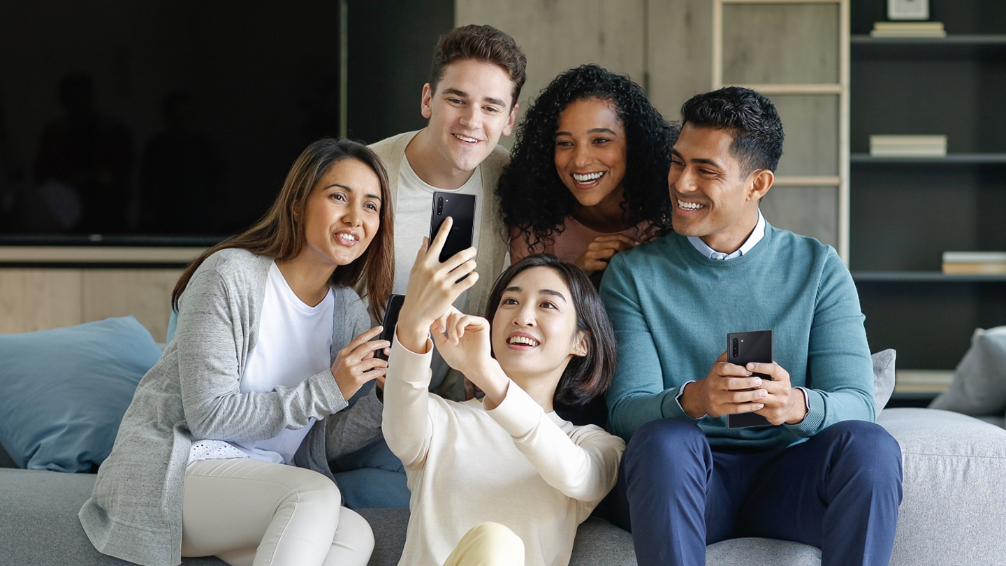 Five mixed adults of a multi-racial race are enjoying watching their cell phones.