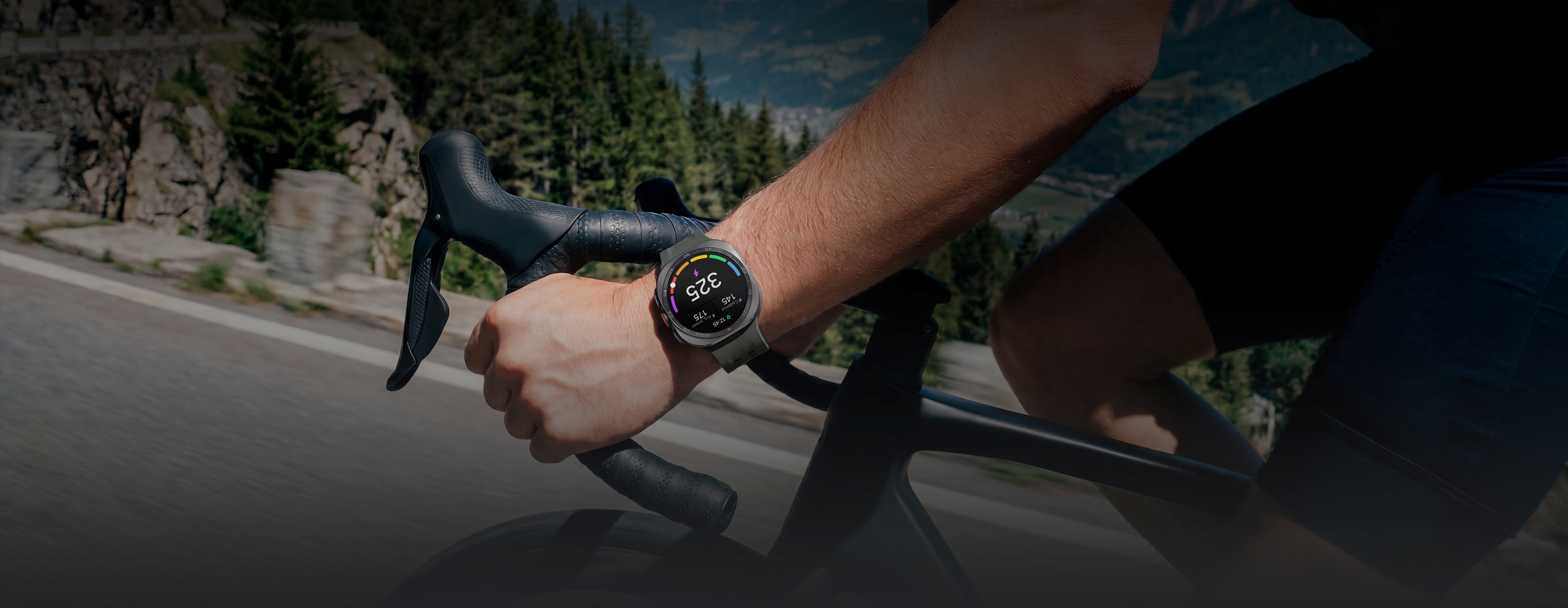 A cyclist is riding a bike on a road in the mountains while wearing a Galaxy Watch Ultra2 in Titanium Silver with a Marine Band in Olive displaying a personalized Functional Threshold Power with cadence and average power.
