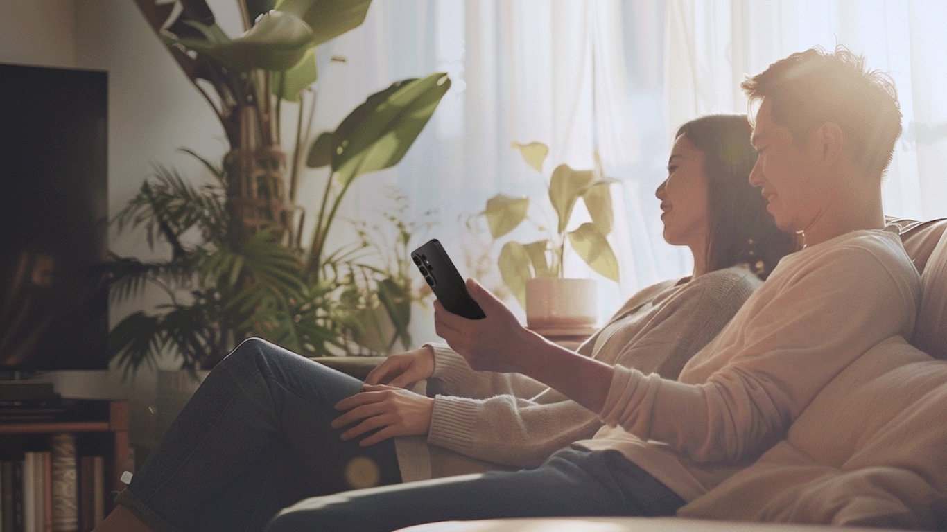 Couple relaxing on a sofa, watch smartphone in a bright living room with plants
