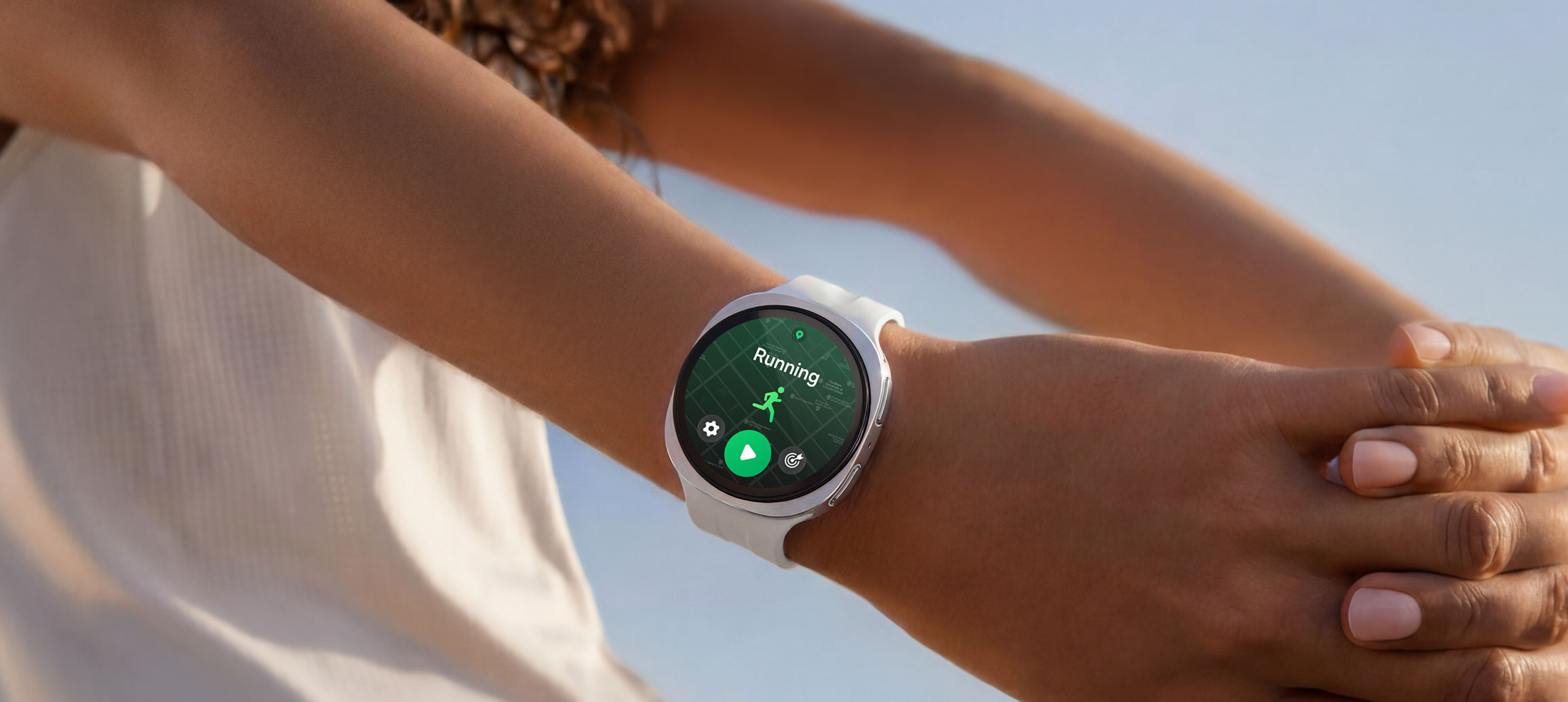 Žmogus dėvi sidabro spalvos „Galaxy Watch9“ &nbsp;su kremine sportine apyranke, tempdamas rankas, o laikrodžio ekrane atverta bėgimo treniruočių programa. 