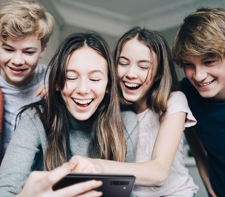 Unos amigos están sentados y se ríen mientras miran un teléfono inteligente.