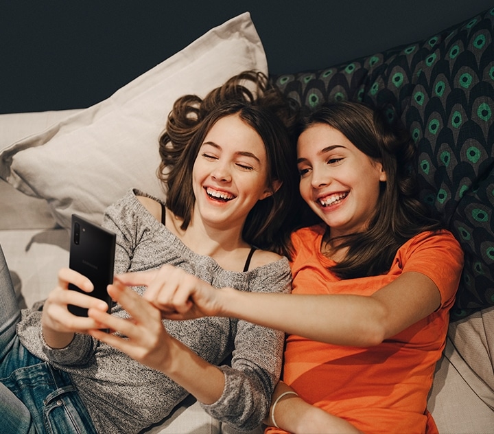 Two women lying down together smiling and looking at their smartphones.