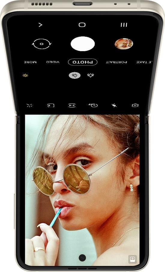 Galaxy Z Flip3 5G upside down in Flex mode, with the Camera interface on the Main Screen. A woman's face is seen in the viewfinder.