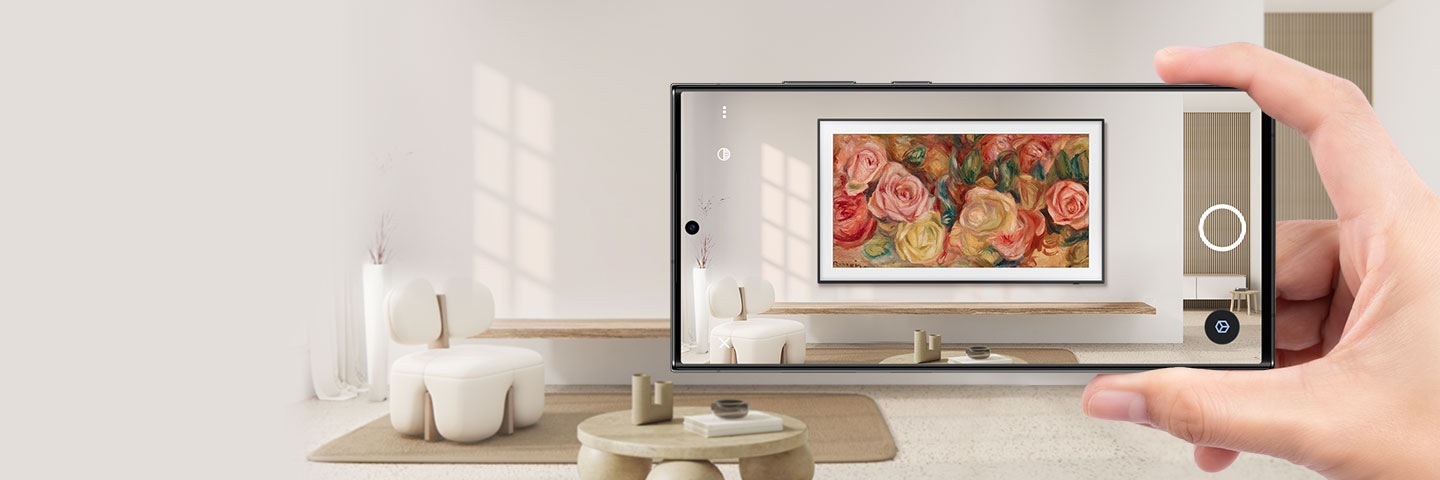 Une main tient un smartphone dans un salon. L’écran du smartphone montre comment The Frame est installé sur le mur en RA.