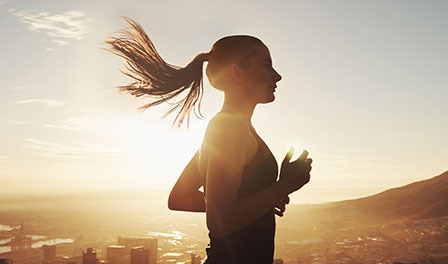 Une femme courant au soleil levant. Ses cheveux flottent dans le vent, témoignant d'un mouvement dynamique.