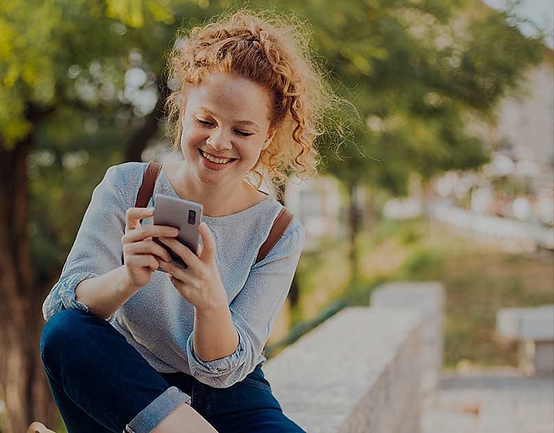 En ung kvinne smiler mens hun ser på smarttelefonen sin.