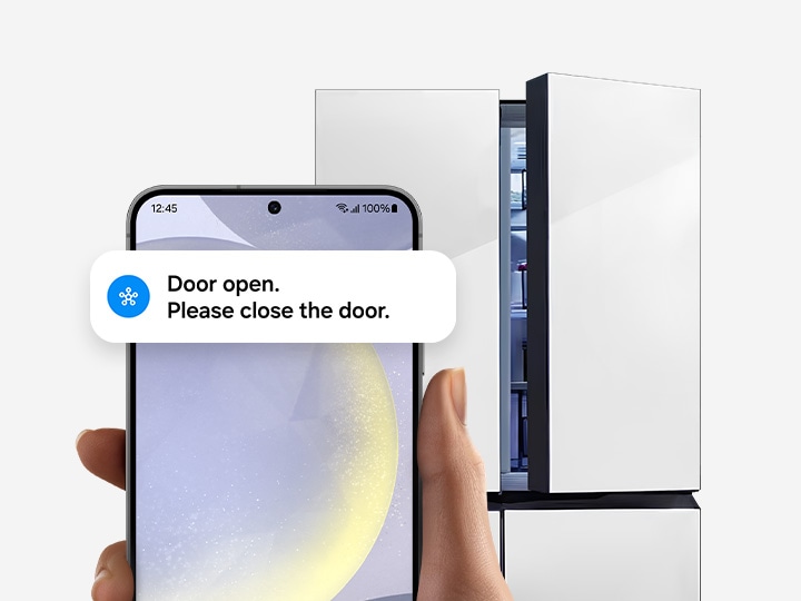 In front of a refrigerator, a hand holds a Galaxy smartphone displaying the SmartThings app UI with Door open notification.