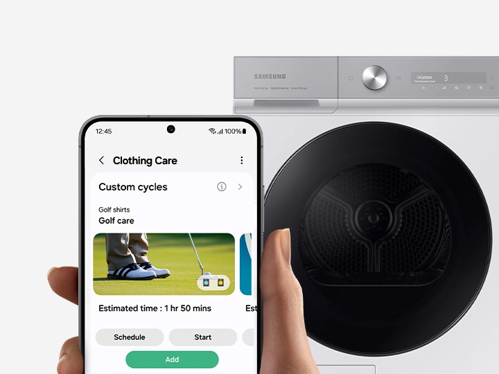 In front of a washing machine, a hand holds a Galaxy smartphone displaying the clothing care SmartThings app UI.