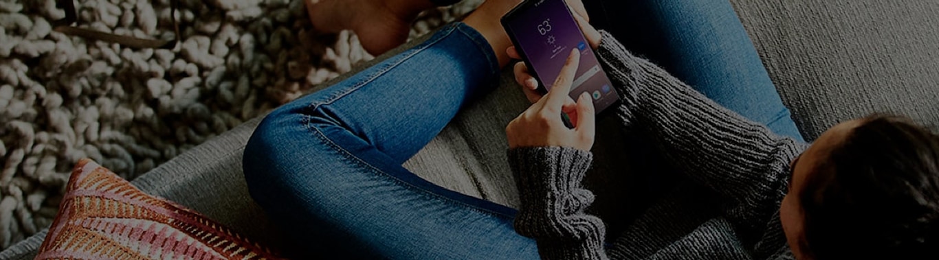 Imagen de una mujer sentada en un sillón revisando su teléfono Galaxy