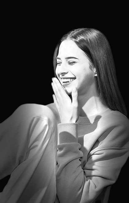 A woman laughing in a laundromat, taken in Portrait Mode with Low-key Mono effect applied.